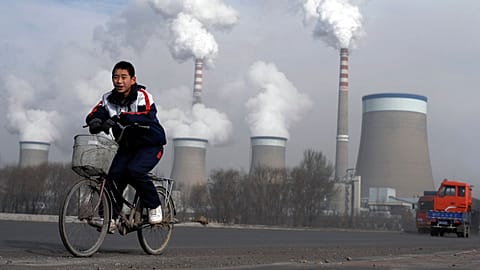 FILE - A boy cycles past a cooling towers of a coal-fired power plant in Dadong, Shanxi province, China, 3 Dec. 2009.