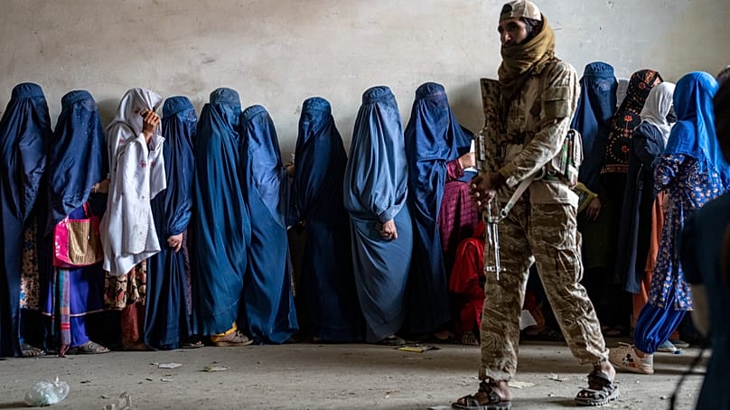 Ein Taliban-Kämpfer steht Wache, während Frauen warten, Lebensmittelrationen zu erhalten, Kabul, Afghanistan, 23. Mai 2023.