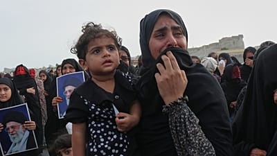 امرأة تحمل طفلاً تبكي خلال جنازة جماعية للأشخاص الذين قتلوا عندما أصاب صاروخ منزلاً كان يقام فيه حفل زفاف في كوهستاك بجنوب إيران