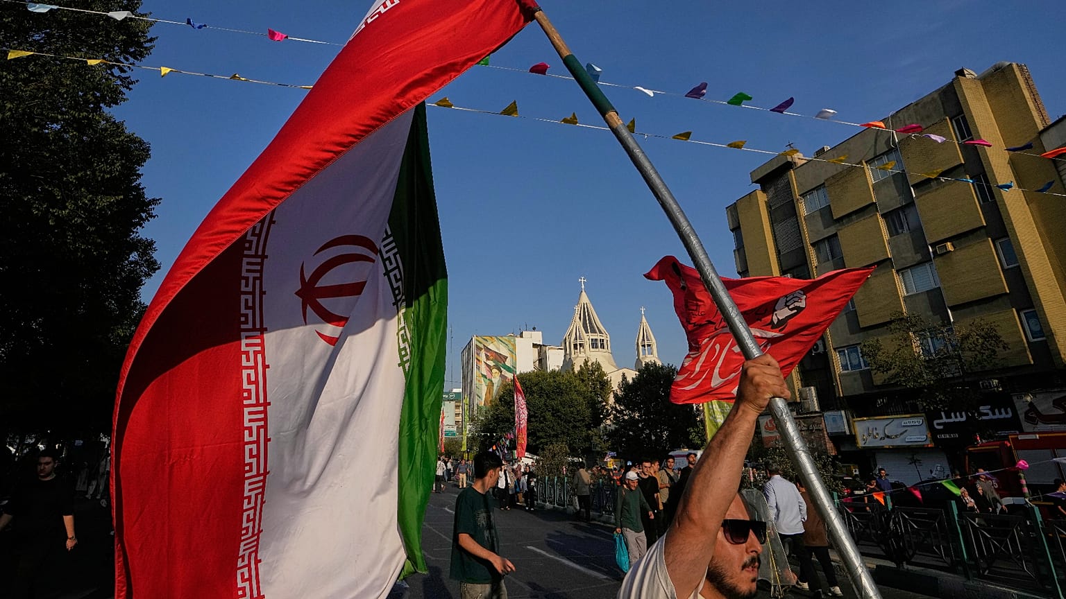 رجل يحمل العلم الإيراني خلال احتفال في الشارع بمناسبة عيد ميلاد النبي محمد، مع كاتدرائية القديس سركيس الأرمنية في الخلفية، في طهران، الأحد 30 أغسطس 2026