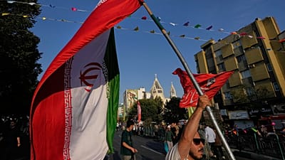رجل يحمل العلم الإيراني خلال احتفال في الشارع بمناسبة عيد ميلاد النبي محمد، مع كاتدرائية القديس سركيس الأرمنية في الخلفية، في طهران، الأحد 30 أغسطس 2026