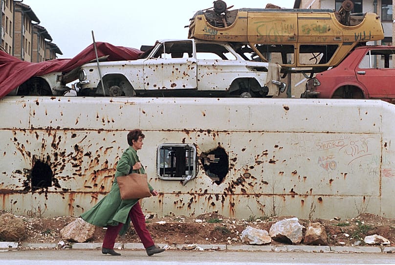 FILE: A woman walks next to a barricade made of mortar and damaged vehicles as she makes her way through the frontline neighbourhood of Dobrinja in Sarajevo, 13 November 1994