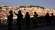ARCHIVE (25.05.2016): Tourists taking photos, with Lisbon's historic centre lit by the sunset in the background.