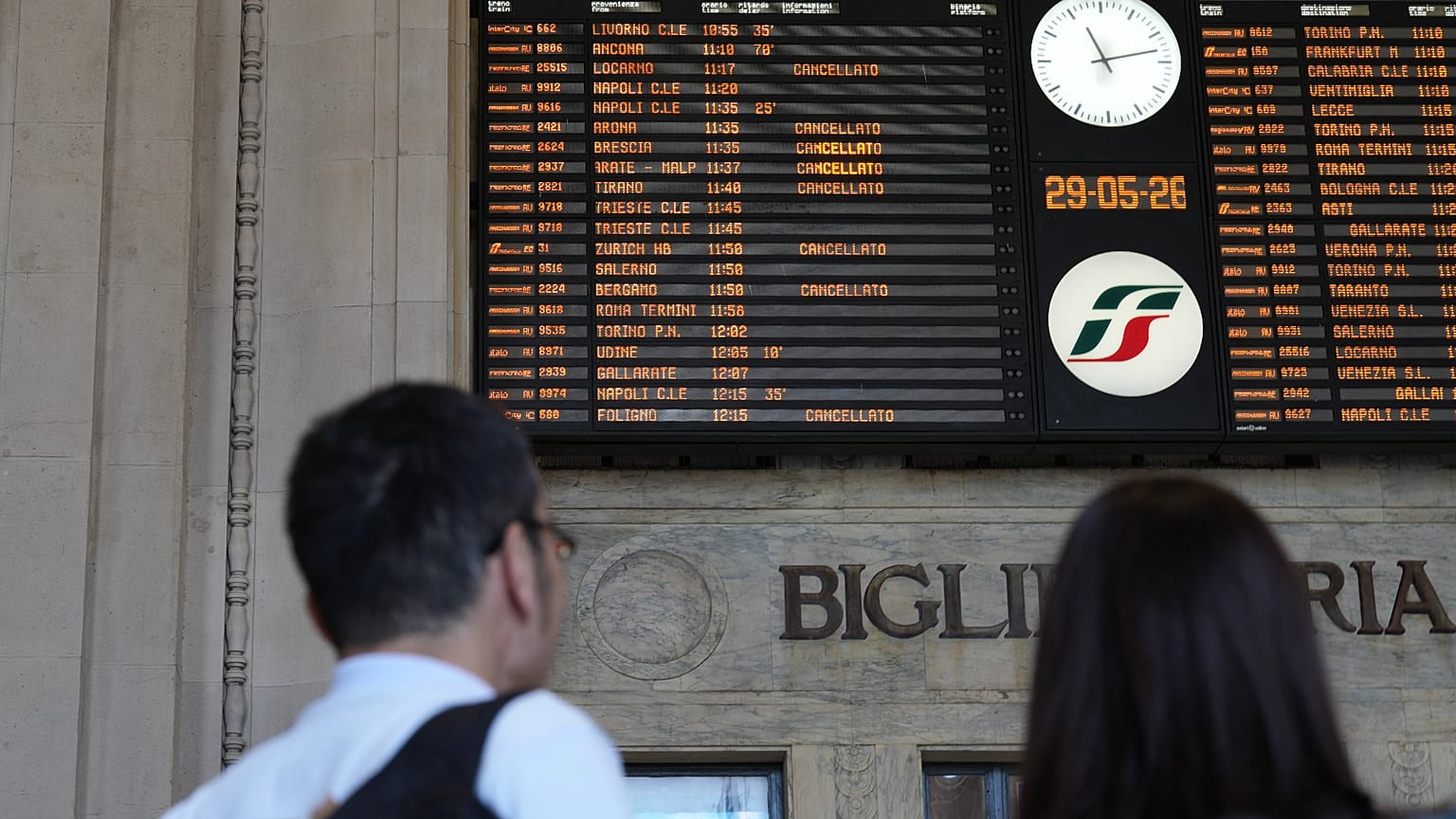 A couple stands in front of a billboard displaying canceled trains during a nationwide general strike called by the labor unions, in Milan, Italy, Friday, May 29, 2026. (AP Ph