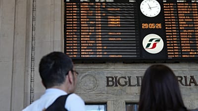 A couple stands in front of a billboard displaying canceled trains during a nationwide general strike called by the labor unions, in Milan, Italy, Friday, May 29, 2026. (AP Ph