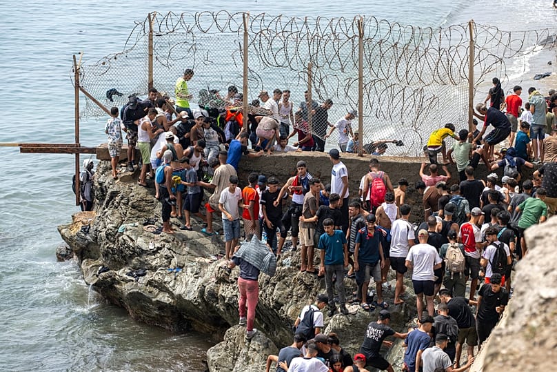 Des personnes franchissent des barbelés alors qu'elles tentent de passer de la ville de Fnideq, au nord du Maroc, à l'enclave espagnole de Ceuta, le vendredi 31 juillet 2026