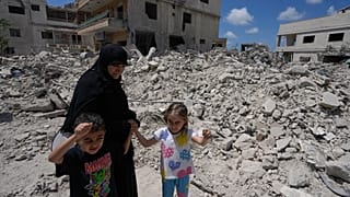 امرأة برفقة أطفالها أمام منزلهم المدمر لدى عودتهم إلى بلدة دير قانون جنوبي لبنان، 15 حزيران 2026.