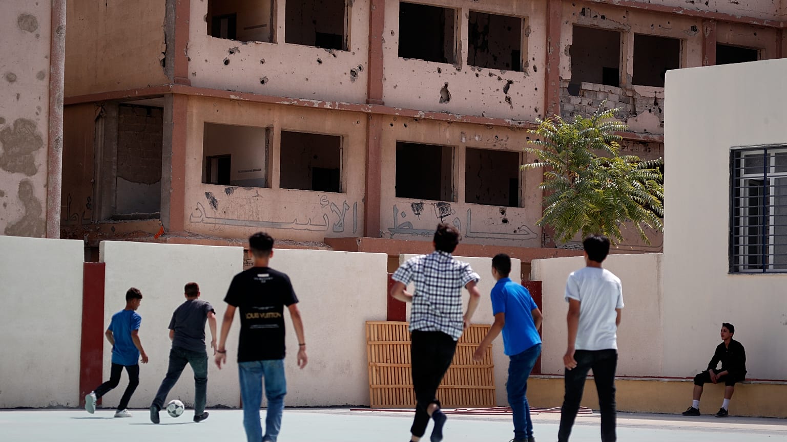يلعب الطلاب كرة القدم في فناء مدرسة تم ترميمها، ويظهر في الخلفية مبنى متضرر يحمل كتابات جدارية تمجد الرئيس السابق حافظ الأسد، في ضاحية دوما بدمشق، سوريا، الخميس 25 سبتمبر 2025