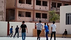 يلعب الطلاب كرة القدم في فناء مدرسة تم ترميمها، ويظهر في الخلفية مبنى متضرر يحمل كتابات جدارية تمجد الرئيس السابق حافظ الأسد، في ضاحية دوما بدمشق، سوريا، الخميس 25 سبتمبر 2025