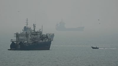 A motorboat travels past commercial vessels anchored amid haze in the Strait of Hormuz off Bandar Abbas, Iran, Monday, Sept. 7, 2026.