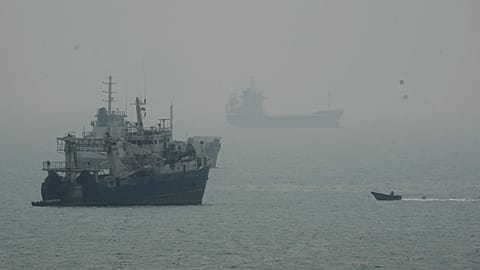 A motorboat travels past commercial vessels anchored amid haze in the Strait of Hormuz off Bandar Abbas, Iran, Monday, Sept. 7, 2026.