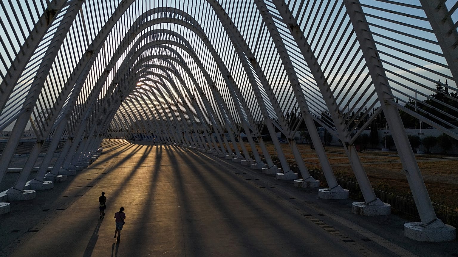 Two girls ride their scooters inside the modern Agora walkway as the sun sets at the main Olympic complex in Athens, 5 August, 2025