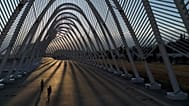 Two girls ride their scooters inside the modern Agora walkway as the sun sets at the main Olympic complex in Athens, 5 August, 2025