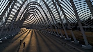 Two girls ride their scooters inside the modern Agora walkway as the sun sets at the main Olympic complex in Athens, 5 August, 2025