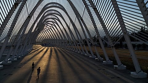 Two girls ride their scooters inside the modern Agora walkway as the sun sets at the main Olympic complex in Athens, 5 August, 2025