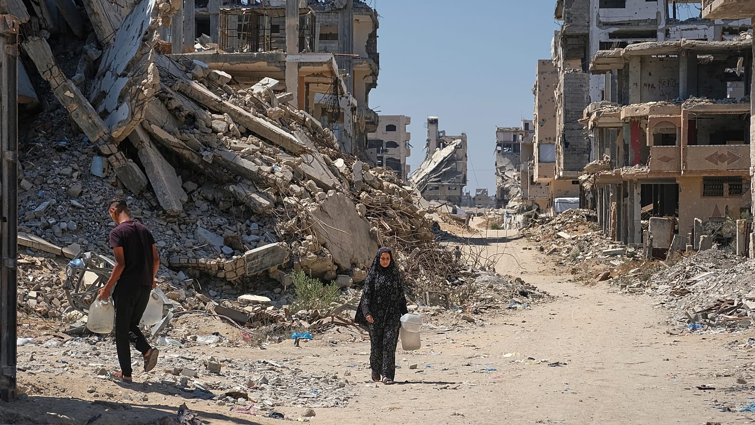 يحمل الفلسطينيون عبوات مياه أثناء سيرهم وسط أنقاض المباني التي دمرتها الغارات الجوية الإسرائيلية خلال الحرب مع حماس، في مدينة غزة، يوم الاثنين 24 أغسطس 2026.