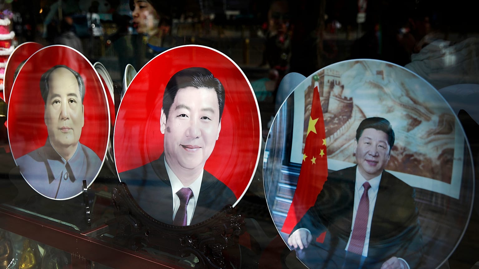 In this March 4, 2015 photo, a woman stands near the souvenir plates bearing images of Chinese President Xi Jinping on display next to late Chinese leader Mao Zedong, left, at