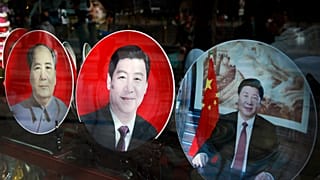 In this March 4, 2015 photo, a woman stands near the souvenir plates bearing images of Chinese President Xi Jinping on display next to late Chinese leader Mao Zedong, left, at