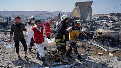 عمال الدفاع المدني ورجل إطفاء يزيلون جثة من موقع انفجار في ما قالت وزارة الدفاع السورية إنه مستودع يستخدم للتخزين المؤقت للأسلحة بالقرب من سرمدا بمحافظة إدلب بسوريا