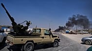 A pickup truck fitted with an anti-aircraft gun is parked across a road as smoke rises after an explosion at a weapons depot near Sarmada, 9 September 2026