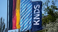 Die Firmenlogos von KNDS neben einer bayerischen und einer deutschen Flagge in München am 22. April 2026