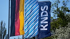 Die Firmenlogos von KNDS neben einer bayerischen und einer deutschen Flagge in München am 22. April 2026