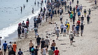 Unas personas caminan por una playa tras intentar cruzar desde la localidad marroquí de Fnideq, en el norte del país, hasta el enclave español de Ceuta, el 31 de julio de 2026
