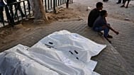 Palestinians sit beside the bodies of members of the Ahmed family, including the parents and their two children, who were killed in an Israeli army strike, at Shifa Hospital i