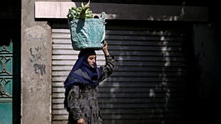تحمل امرأة مصرية سلالاً من الخضروات على رأسها في قرية العور بالقرب من المنيا، على بعد 220 كيلومتراً 