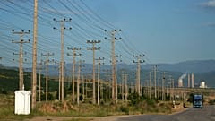 Ένα φορτηγό περνά κοντά σε κολόνες ηλεκτρικού ρεύματος, ενώ ένα εργοστάσιο παραγωγής ενέργειας φαίνεται στο βάθος, έξω από την πόλη Κοζάνη, την Πέμπτη 2 Ιουνίου 2022.