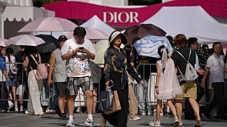 FILE. A woman with her shopping items walks by other shoppers gathering outside a Dior promotion booth in Beijing, 17 Aug. 2026