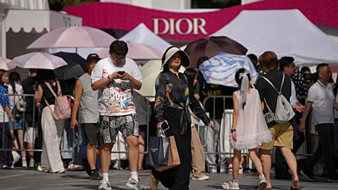 FILE. A woman with her shopping items walks by other shoppers gathering outside a Dior promotion booth in Beijing, 17 Aug. 2026