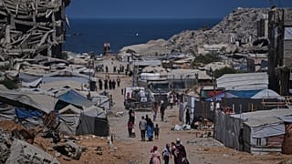 أشخاص يسيرون بمحاذاة خيام تؤوي فلسطينيين نازحين وسط أنقاض مبانٍ دمرتها غارات جوية إسرائيلية خلال الحرب مع حركة حماس، في مدينة غزة، يوم الاثنين 24 أغسطس 2026. (صورة من أسوشيتد 
