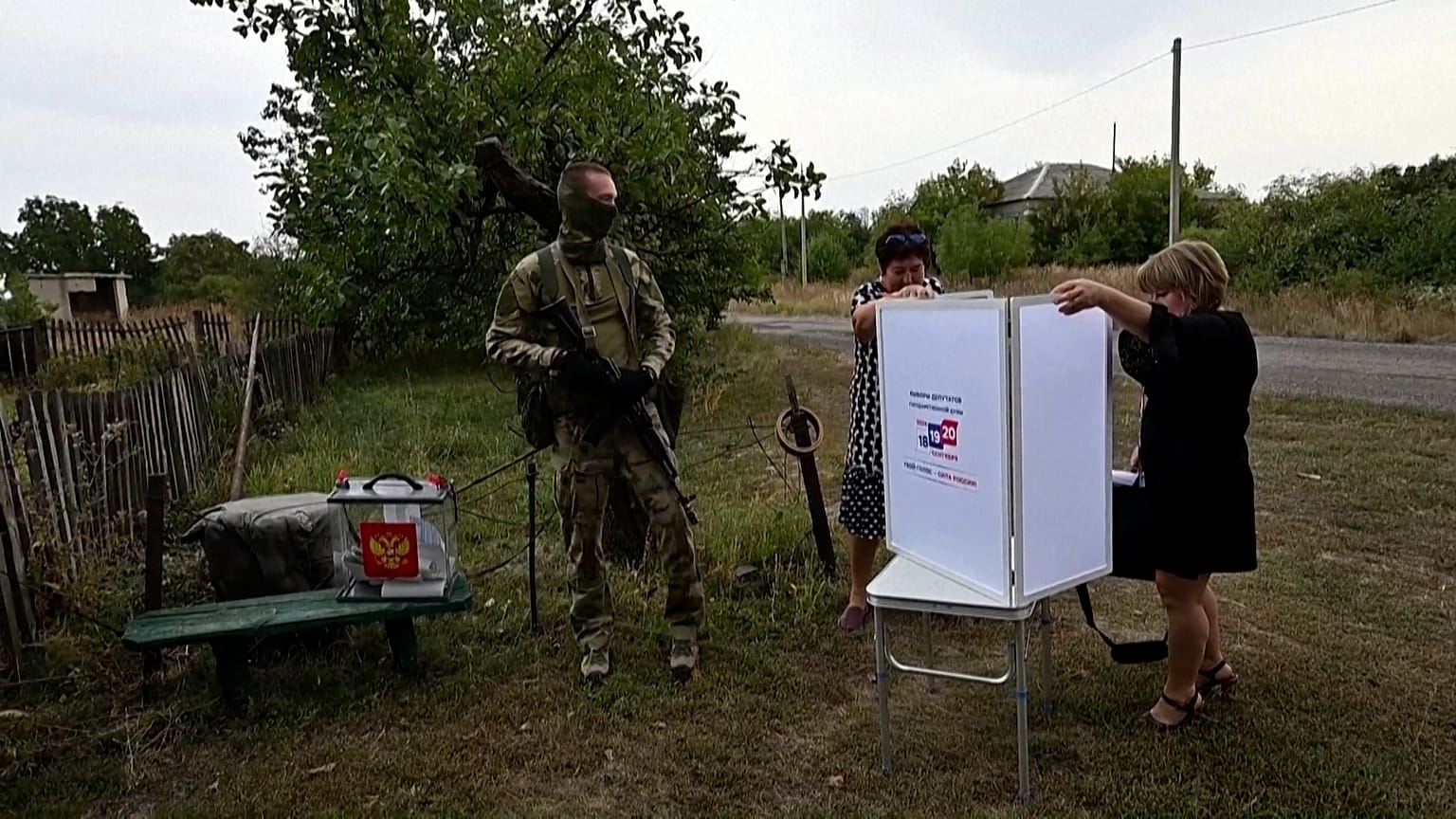 Wählerinnen und Wähler unter Aufsicht eines bewaffneten Mannes in russischer Militäruniform