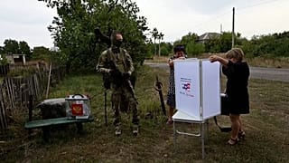 Избиратели под контролем вооружённого мужчины в российской военной форме