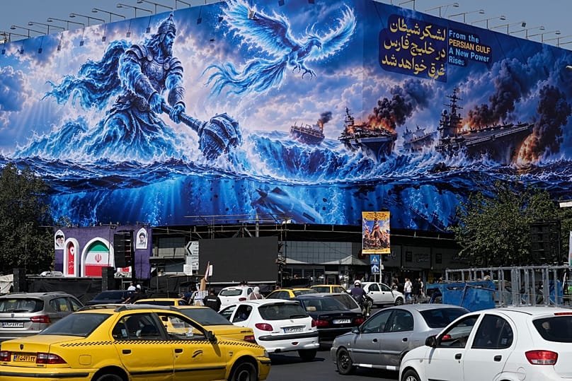 لوحة إعلانية في طهران تُظهر شخصاً يهاجم حاملات طائرات أمريكية، مع عبارة "من الخليج ترتفع قوة جديدة"، في 14 أيلول 2026.