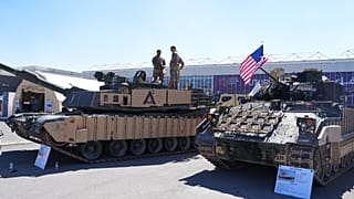 يقف أفراد من الجيش الأمريكي فوق دبابة القتال الرئيسية "إم 1 إيه 2 أبرامز" (M1A2 Abrams)، بينما تُعرض مركبة القتال المشاة "إم 2 إيه 3 برادلي" (M2A3 Bradley) في مكان قريب، وذلك 
