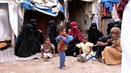 Vertriebene Frauen und Kinder sitzen vor Zelten im Lager Al Kadha auf dem Boden.