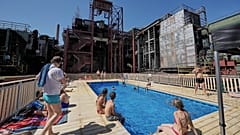 A temporary pool glows blue amidst the industrial backdrop of the world heritage former Zollverein coking plant in Essen, Germany, Friday, Aug. 14, 2026.