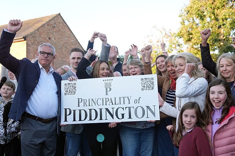 Local residents pose with a "Principality of Piddington" sign in the village of Piddington, Oxfordshire, England