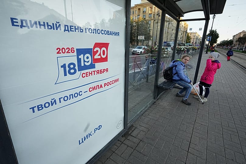 В понедельник, 14 сентября 2026 года, в Санкт-Петербурге люди ждут трамвай на остановке рядом с рекламным щитом, призывающим проголосовать на трехдневных парламентских выборах