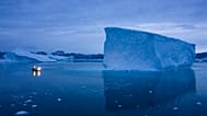 Una barca naviga di notte accanto a grandi iceberg nella Groenlandia orientale.