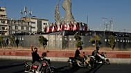 A man reacts to the camera while driving past a monument depicting the clenched fist of the late Iranian Supreme Leader Ayatollah Ali Khamenei, who was killed in the U.S. and 