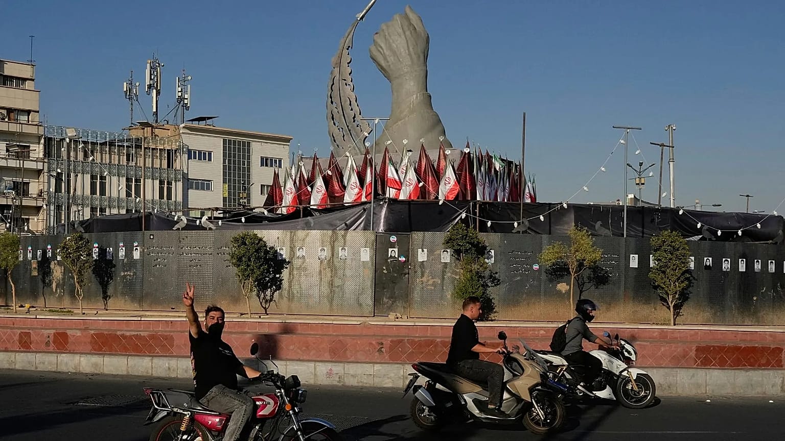 A man reacts to the camera while driving past a monument showing the clenched fist of the late Iranian Supreme Leader Ayatollah Ali Khamenei, who was killed in the US and