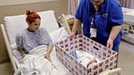 Keyshla Rivera mosolyog újszülött fiára, Jesusra, miközben Christine Weick okleveles ápolónő egy babadobozt mutat be a philadelphiai Temple Egyetemi Kórházból távozása előtt