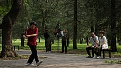 A couple watch a woman practice Tai Chi with a sword at a park near the Temple of Heaven in Beijing.