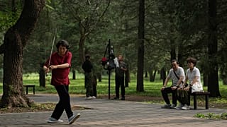 A couple watch a woman practice Tai Chi with a sword at a park near the Temple of Heaven in Beijing.