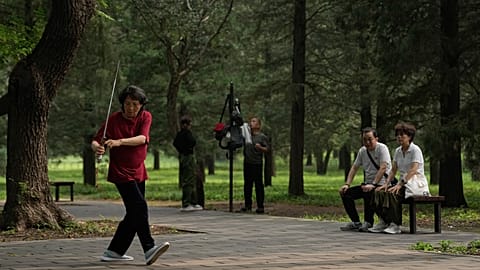 A couple watch a woman practice Tai Chi with a sword at a park near the Temple of Heaven in Beijing.
