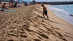 A swimmer walks on the shore of a beach in Barcelona, Spain, Tuesday, July 22, 2025. 