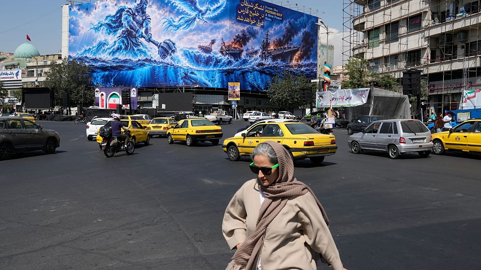 A woman walks past a billboard depicting a Persian legendary hero and flying figure hitting U.S. aircraft carriers alongside the message in English and Farsi: "From the Persia